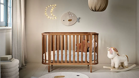 Lit de bébé à barreaux en bois dans chambre d'enfant grise et neutre.